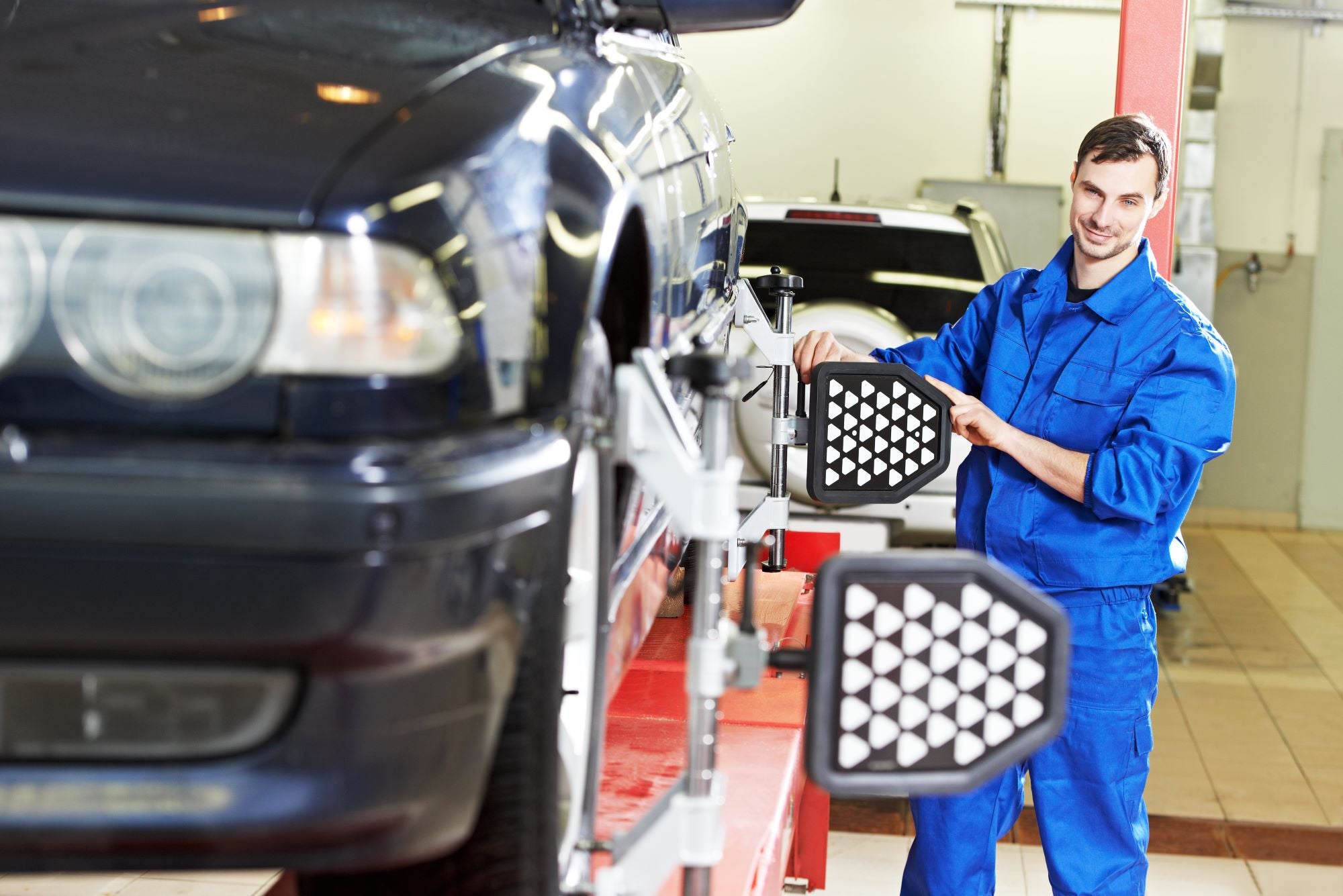 A man in blue overalls stands beside a car, demonstrating proper tire care techniques.